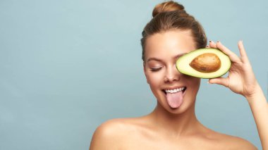 Açık arkaplanda taze avokadosu olan güzel genç bir kadın.