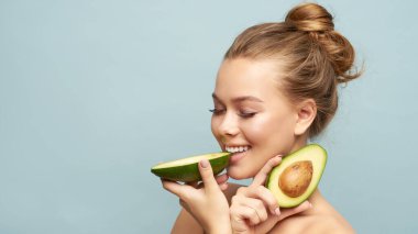 Açık arkaplanda taze avokadosu olan güzel genç bir kadın.