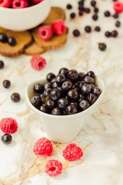 Ham ahududu ve beyaz bardak yaban mersini. beyaz mermer zemin. Yaz meyve, çilek. Detoks diyetler ve sağlıklı gıda kavramı.