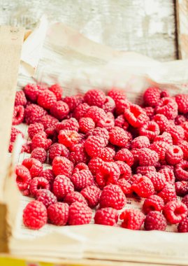 Mavi ahşap bir masa üzerinde bir kutu içinde kırmızı ahududu. Taze çilek. Detoks Diyet ve yaz yiyecek konsepti