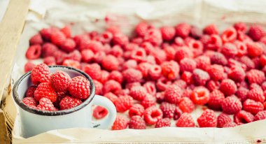 Mavi ahşap bir masa üzerinde bir kutu içinde kırmızı ahududu. Taze çilek. Sağlıklı ve ham antioksidan gıda kavramı.