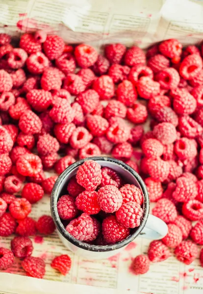 Mavi ahşap bir masa üzerinde bir kutu içinde kırmızı ahududu. Bir demir mug içinde taze çilek. Sağlıklı ve ham antioksidan gıda kavramı.
