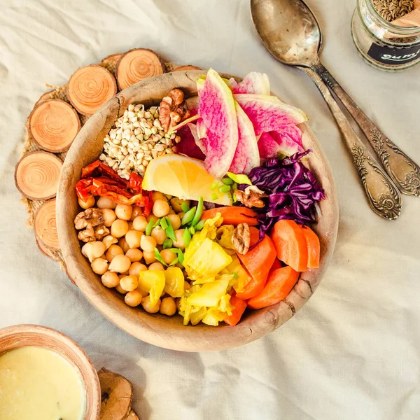 A balanced lunch/dinner - multicolored vegetables, spicy beans (chickpeas), sun-dried tomatoes, lemon, nuts, kimchi with turmeric in wooden dishes