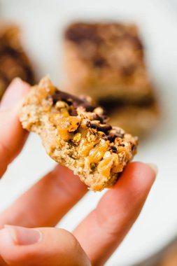Granola bar-pastayla çikolata, beyaz bir kase dilimlenmiş parçaları yığını. Dietic tatlı. Sağlıklı vegan gıda kavramı. Yeme işlemi. Genç bir kadın elinde.
