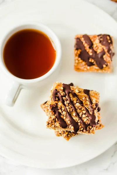 Granola bar with date caramel and chocolate. Healthy sweet dessert snack. Cereal granola bar with nuts, fruit and berries on a white marble table.Top view. A cup of coffee.