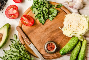 Yeşillik, domates, salatalık, baharat, avokado, sebze, bahar taze yiyecek. Ham salata hazırlanıyor. Ahşap masa, üstten görünüm. Vejetaryen ve vegan gıda kavramı