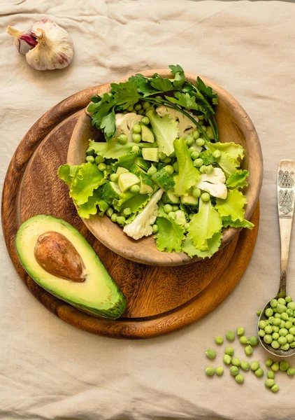 Fresh delicious green salad with avocado in a wooden plate and g — Stock Photo, Image