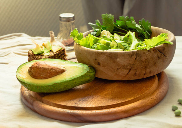 Fresh delicious green salad with avocado in a wooden plate and g