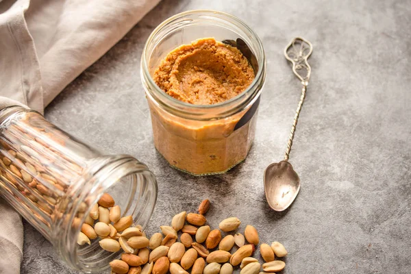 Frische hausgemachte cremige Erdnussbutter in einem Glas auf grauem Backblech — Stockfoto