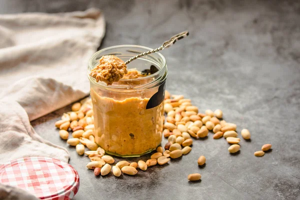 Tartinade d'arachides fraîches dans un bocal et une cuillère et arachides éparpillées sur gr — Photo