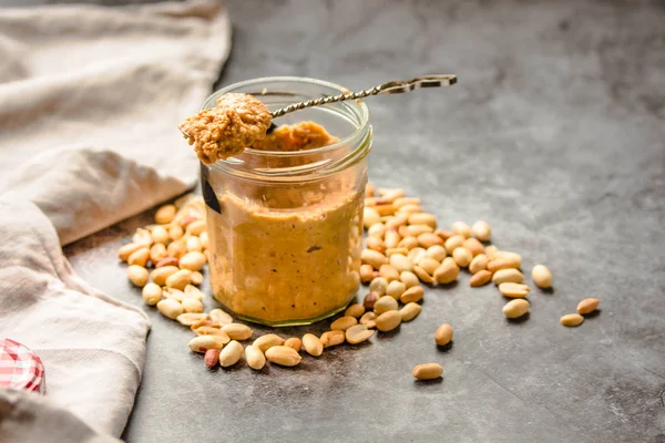 Tartinade d'arachides fraîches dans un bocal et une cuillère et arachides éparpillées sur gr — Photo