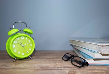 Gri arkaplanlı kitaplarla birlikte yeşil alarmlı saat gösterisi. Sağlıklı bir kavram.