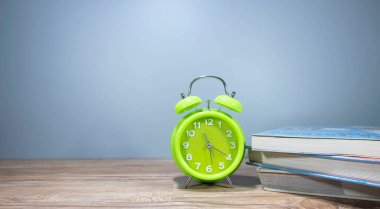 Gri arkaplanlı bir sürü kitabı olan yeşil çalar saat. Sağlıklı bir kavram.