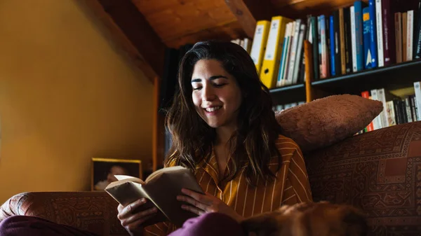 Mujer Joven Sonriendo Mientras Lee Libro Sofá —  Fotos de Stock