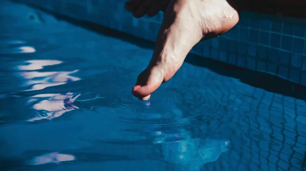 Foot skimming the blue water of a swimming pool
