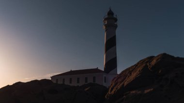 Gün batımında kayaların arkasında deniz feneri
