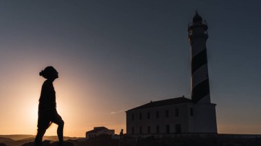 Gün batımında fenere bakan genç bir kadının siyah ışığı.