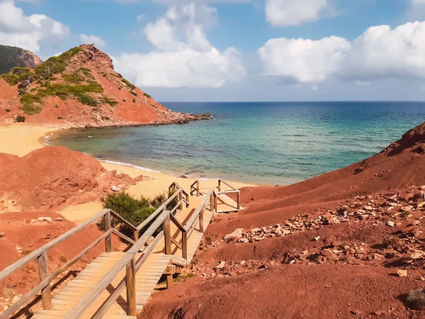 Stairs leading to a deserted red sand beach