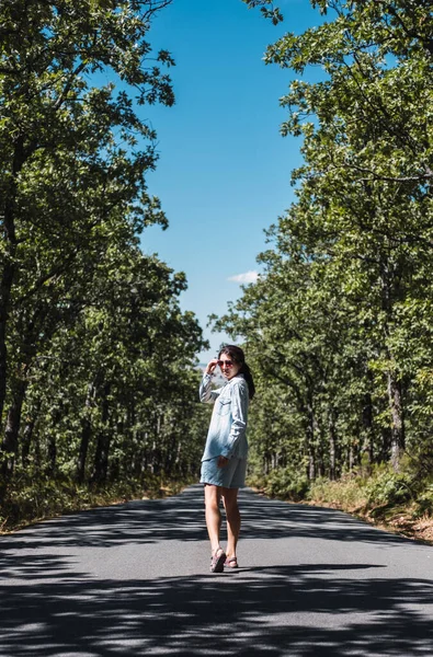 Genç bir kadın ağaçlarla dolu bir yolda yürüyor.