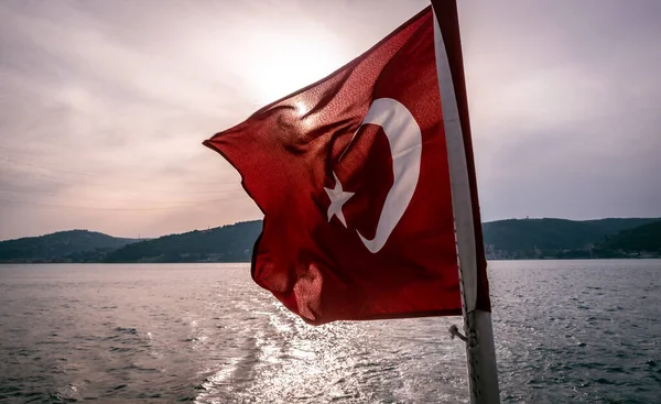 Arkasında güneş olan bir Türk bayrağı sallıyor, teknenin arkasında, rüzgarla denizin üzerinde kayıyor. Hilal ve yıldızlı kırmızı bayrak.