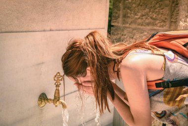 Genç bir kadın yaz sıcağında sokak çeşmesinde yüzünü yıkayarak serinliyor..