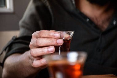 Elinde bir fincan Türk çayı tutan bir adam, sadece eller, ön planda ikinci çay bardağı..