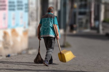 Süpürgesi ve faraşı ile ıssız bir yolda yürüyen, izole edilmiş ve bulanık bir arka planı olan bir temizlikçi.. 