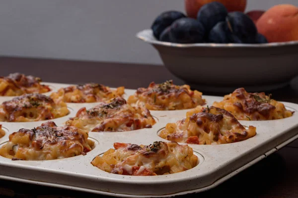 Fırında eritilmiş çedar peyniri sosuyla servis edilecek makarna topları ve bulanık arkaplanda biraz meyve..