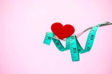 Diyet kilo kaybı, teyp ve kırmızı kalp şekli için açık pembe renkli çatalı ile ölçmek için sağlıklı beslenme kavramı dikkat çekmek