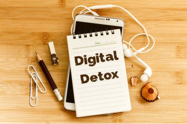 Dijital Detox metni ve kalemi olan bir not defteri, ahşap masadaki akıllı telefon, üstten çekim veya üstten görüntü, bağlantısız internet yaşam tarzı konsepti