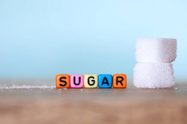 Küp beyaz şeker ve şeker kelime ile açık mavi renkli ahşap masa, 14 Kasım Dünya Diyabet günü kampanyası için sağlıksız yiyecek konsepti bloğunu renkli alfabesi