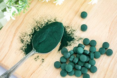 Spiulina tozu ve spirulina haplarını kaşığa doldur. Sağlıklı beslenme ve detoks konsepti.