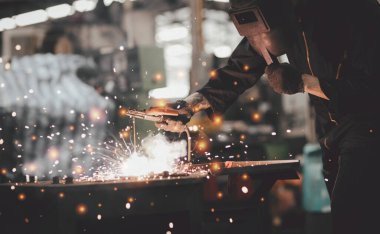 Fabrikadaki çelik yapının elektrik tekerleği öğütülmesi, metal kaynak ve kıvılcımlar yapan koruyucu maskeli bir işçi.