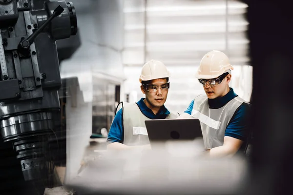 两名30多岁的亚洲工人在一家金属制造厂工作 戴着安全帽 戴着防护眼镜 那个指点笔记本电脑 谈论现代工厂新计划的人 — 图库照片