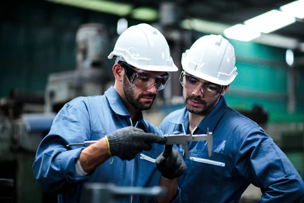 Two maintenance engineers discuss inspect relay checking information and protection system on a tablet computer in a factory. They work a heavy industry manufacturing factory.