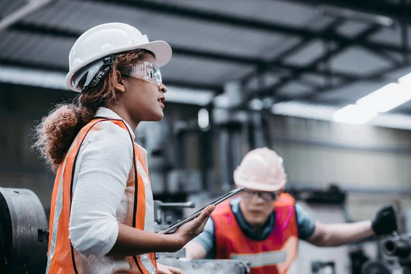 女工业工程师头戴白色头盔 站在一家重工业工厂的后面 与工人们交谈 — 图库照片