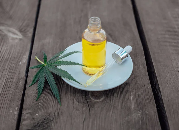Glass bottle and dropper CBD OIL, THC tincture and cannabis leaf on wooden background. Laboratory Production of cosmetics with CBD oil.