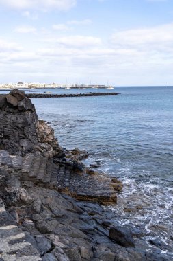 Lanzarote 'de sakin bir kıyı sahnesi. Volkanik kayaların bulutlu bir gökyüzünün altında dingin okyanusla buluşması..