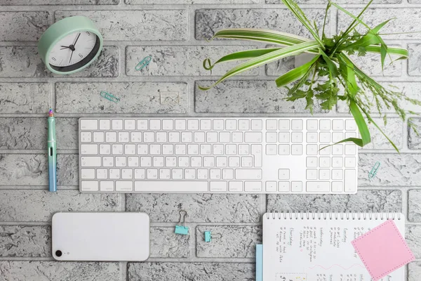 キーボード ペーパークリップ 植物や時計付き花瓶とオフィスデスクでトップビュー 灰色のレンガの背景にフラットレイアウト — ストック写真