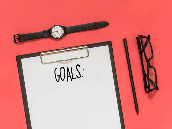 Top view goals list with notebook, glasses, watch, pencil on pink background with blank space for text. Flat lay. Copy space.