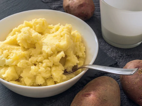 Puree. Mashed potatoes in a white plate, fresh potato, milk in a white Cup. Grey background