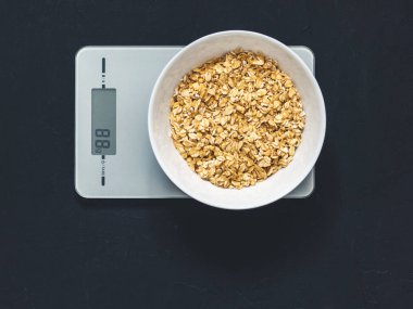 Diyet kavramı, doğru beslenme, sağlıklı yemek. Yulaf ezmesi mutfak terazisi üzerinde beyaz bir tabak içinde. Ürünler ağırlığında. Kahvaltı, üstten görünüm