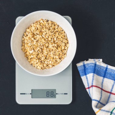 Diyet kavramı, doğru beslenme, sağlıklı yemek. Yulaf ezmesi mutfak terazisi üzerinde beyaz bir tabak içinde. Ürünler ağırlığında. Kahvaltı, üstten görünüm