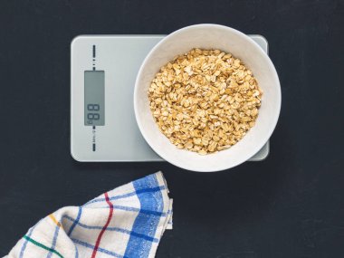 Diyet kavramı, doğru beslenme, sağlıklı yemek. Yulaf ezmesi mutfak terazisi üzerinde beyaz bir tabak içinde. Ürünler ağırlığında. Kahvaltı, üstten görünüm