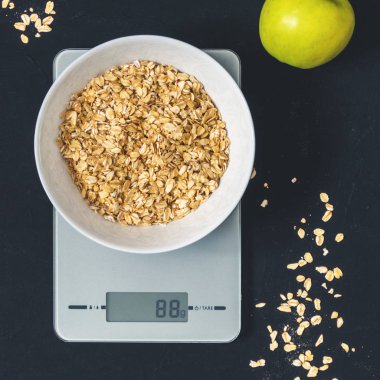 Diyet kavramı, doğru beslenme, sağlıklı yemek. Yulaf ezmesi mutfak terazisi üzerinde beyaz bir tabak içinde. Ürünler ağırlığında. Kahvaltı, üstten görünüm