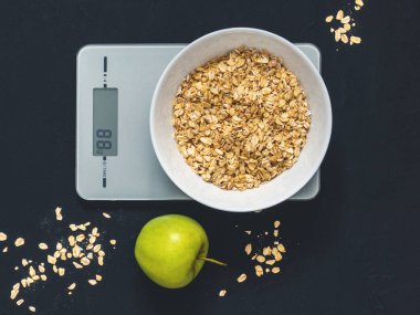 Diyet kavramı, doğru beslenme, sağlıklı yemek. Yulaf ezmesi mutfak terazisi üzerinde beyaz bir tabak içinde. Ürünler ağırlığında. Kahvaltı, üstten görünüm