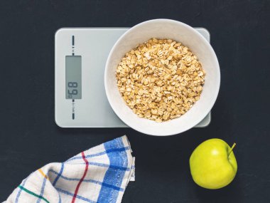 Diyet kavramı, doğru beslenme, sağlıklı yemek. Yulaf ezmesi mutfak terazisi üzerinde beyaz bir tabak içinde. Ürünler ağırlığında. Kahvaltı, üstten görünüm