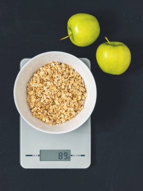 Diyet kavramı, doğru beslenme, sağlıklı yemek. Yulaf ezmesi mutfak terazisi üzerinde beyaz bir tabak içinde. Ürünler ağırlığında. Kahvaltı, üstten görünüm