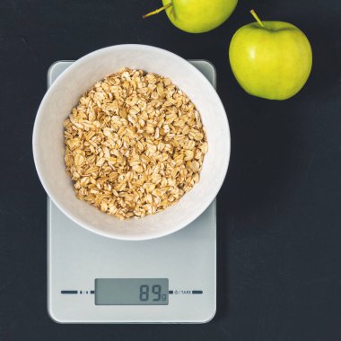 Diyet kavramı, doğru beslenme, sağlıklı yemek. Yulaf ezmesi mutfak terazisi üzerinde beyaz bir tabak içinde. Ürünler ağırlığında. Kahvaltı, üstten görünüm