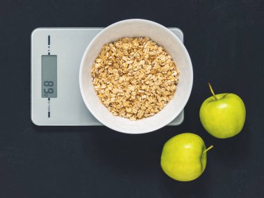 Diyet kavramı, doğru beslenme, sağlıklı yemek. Yulaf ezmesi mutfak terazisi üzerinde beyaz bir tabak içinde. Ürünler ağırlığında. Kahvaltı, üstten görünüm